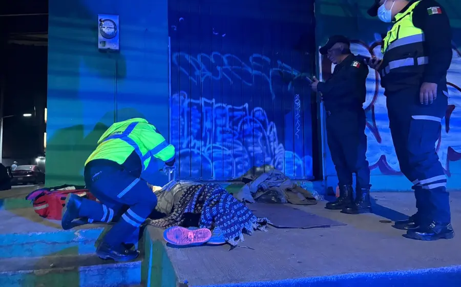 Una mujer en situación de calle yace sin vida sobre la banqueta en la vía pública, evidenciando una lamentable situación de abandono.