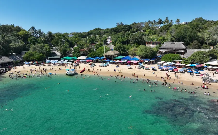 Una concurrida playa de la costa de Oaxaca, llena de turistas que disfrutan del mar y la arena durante el primer puente vacacional del año.