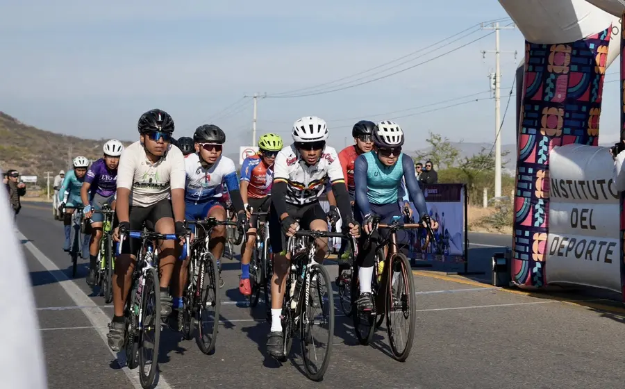 Un grupo de ciclistas avanza en formación durante una competencia de ciclismo de ruta, componiendo uno de los bloques de competidores.