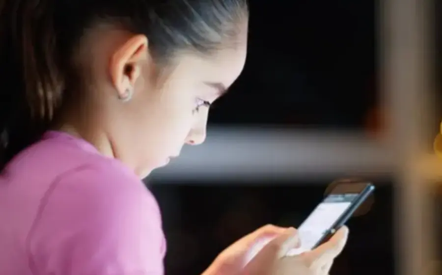 Un niño en una habitación oscura es iluminado por la luz de una tableta, ilustrando cómo la sobreexposición digital afecta los procesos del sueño y el cerebro.