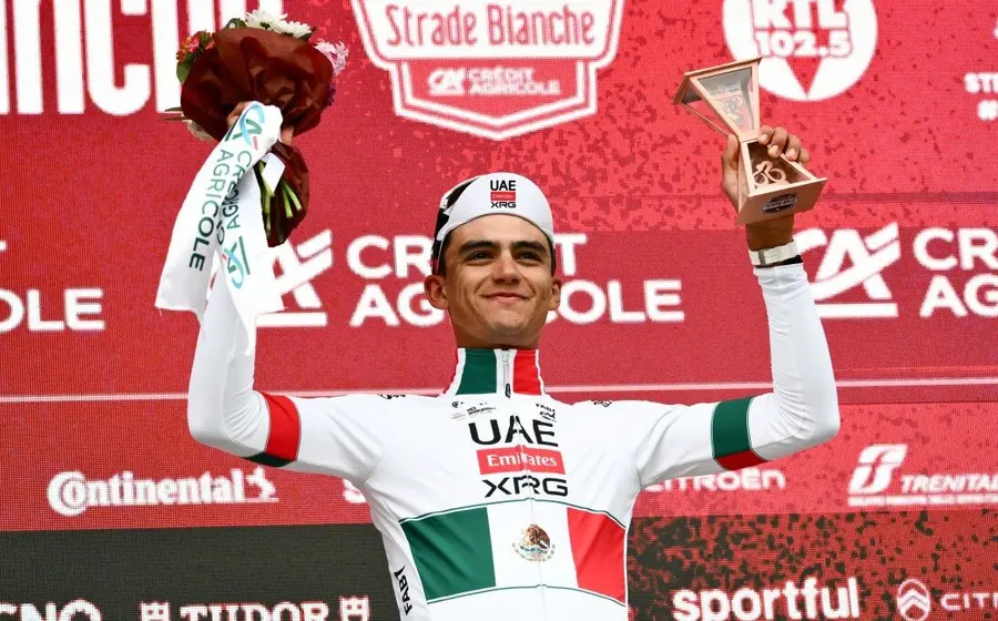 El ciclista mexicano Isaac del Toro celebra en el podio después de obtener el histórico tercer lugar en la carrera Strade Bianche.