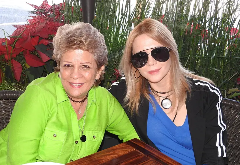 Adriana Hurtado y Marcela Mendiola posan juntas y sonrientes para la cámara durante un evento social, compartiendo un momento feliz.