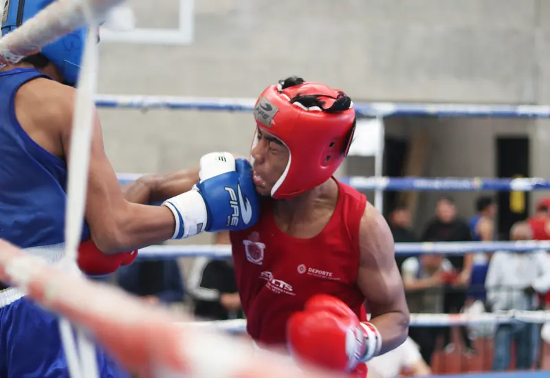 Dos jóvenes pugilistas intercambian golpes durante un duro combate de boxeo en la Olimpiada Estatal celebrada en el Gimnasio Ricardo Flores Magón.