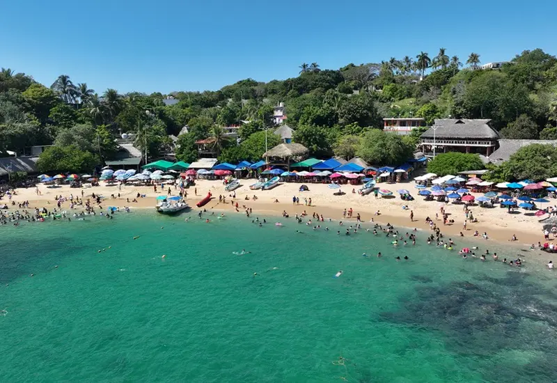 Una concurrida playa de la costa de Oaxaca, llena de turistas que disfrutan del mar y la arena durante el primer puente vacacional del año.