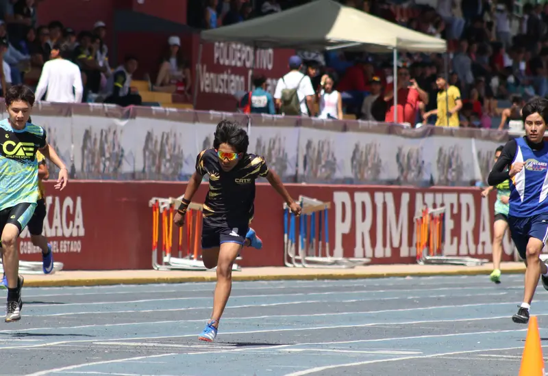 Un atleta cruza la línea de meta con gran esfuerzo y determinación durante una competencia de la Olimpiada Estatal de Atletismo.