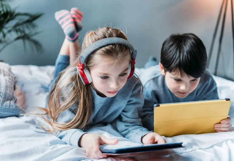 Un niño se entretiene viendo contenidos audiovisuales en una tableta, reflejando una de las actividades recreativas infantiles más comunes actualmente.