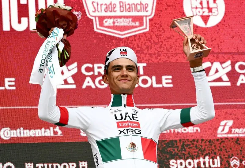 El ciclista mexicano Isaac del Toro celebra en el podio después de obtener el histórico tercer lugar en la carrera Strade Bianche.